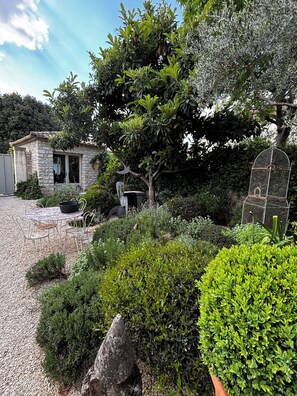 A stone building with a garden, a metal table with chairs, and a birdcage. - Charming apartment-comfort and elegance-St Rémy De Provence-5 mn from town center (Saint-Rémy-de-Provence)