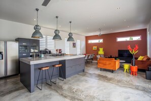 A modern kitchen with bar stools, a dining area with a sofa, and a TV in a living room. - Luxury 5 star Villa with private pool 600 m from Jan Thiel Beach (Jan Thiel)