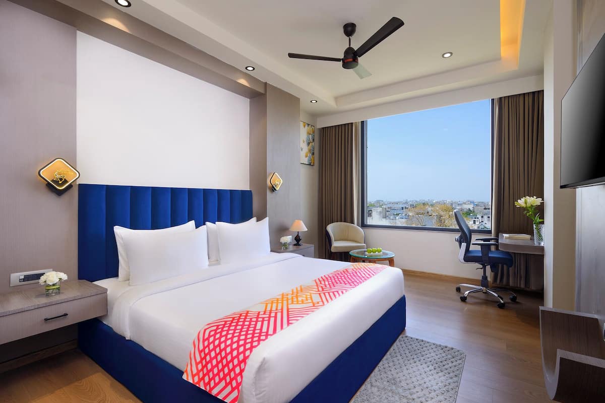 Quarto de hotel com uma cama grande, escrivaninha, cadeira, televisão e vista para a cidade.