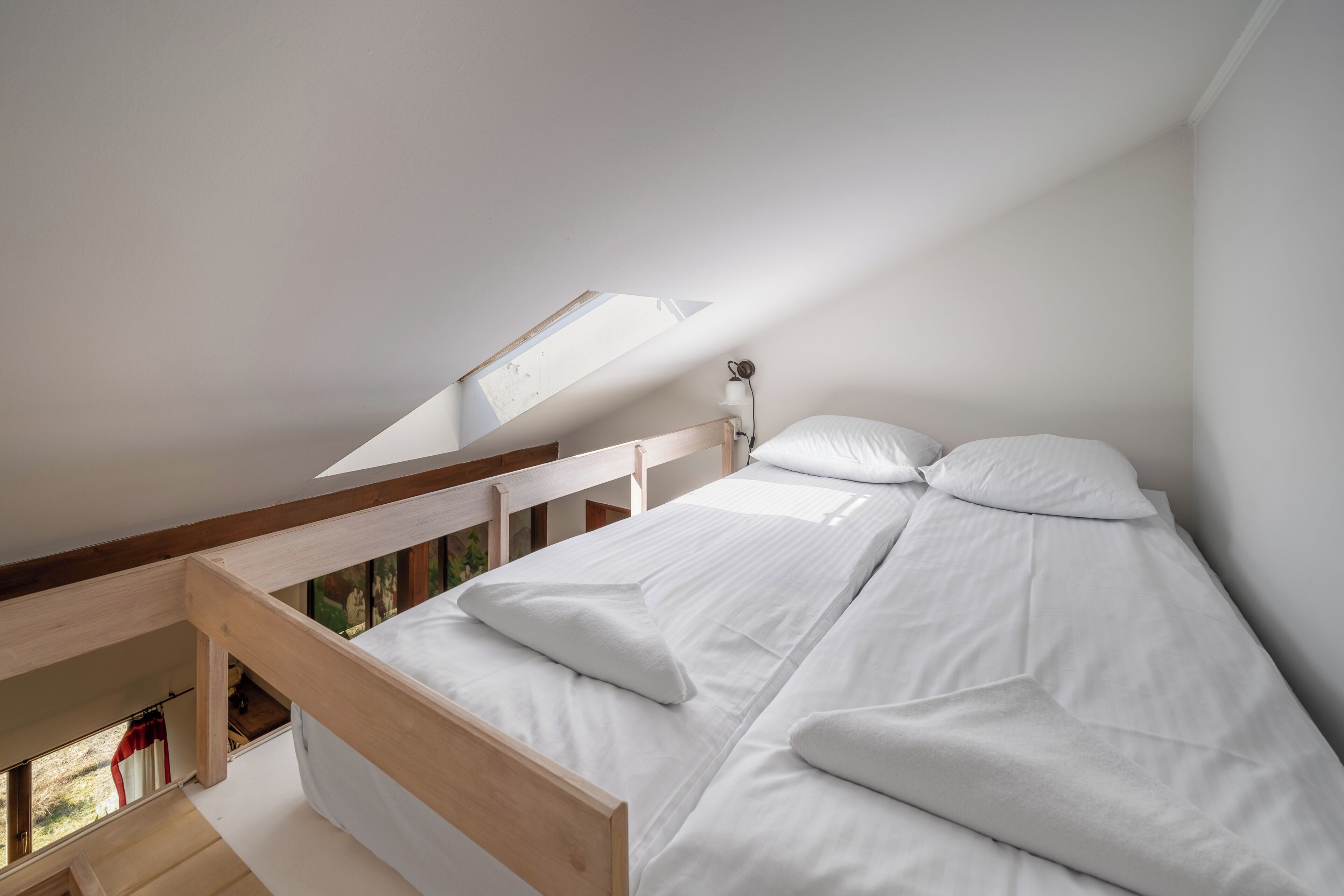 Ein Schlafzimmer mit Dachfenster, Holzbettgestell, weißer Bettwäsche und Blick ins Freie.