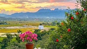 A wooden deck with a table and chairs, overlooking a scenic landscape with mountains and fields.