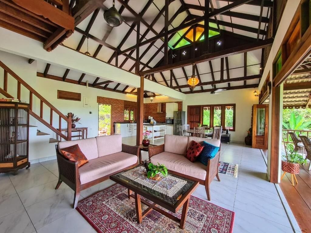 A spacious living area with a high ceiling, wooden beams, a sofa set, a coffee table, and a view of the kitchen in the background.