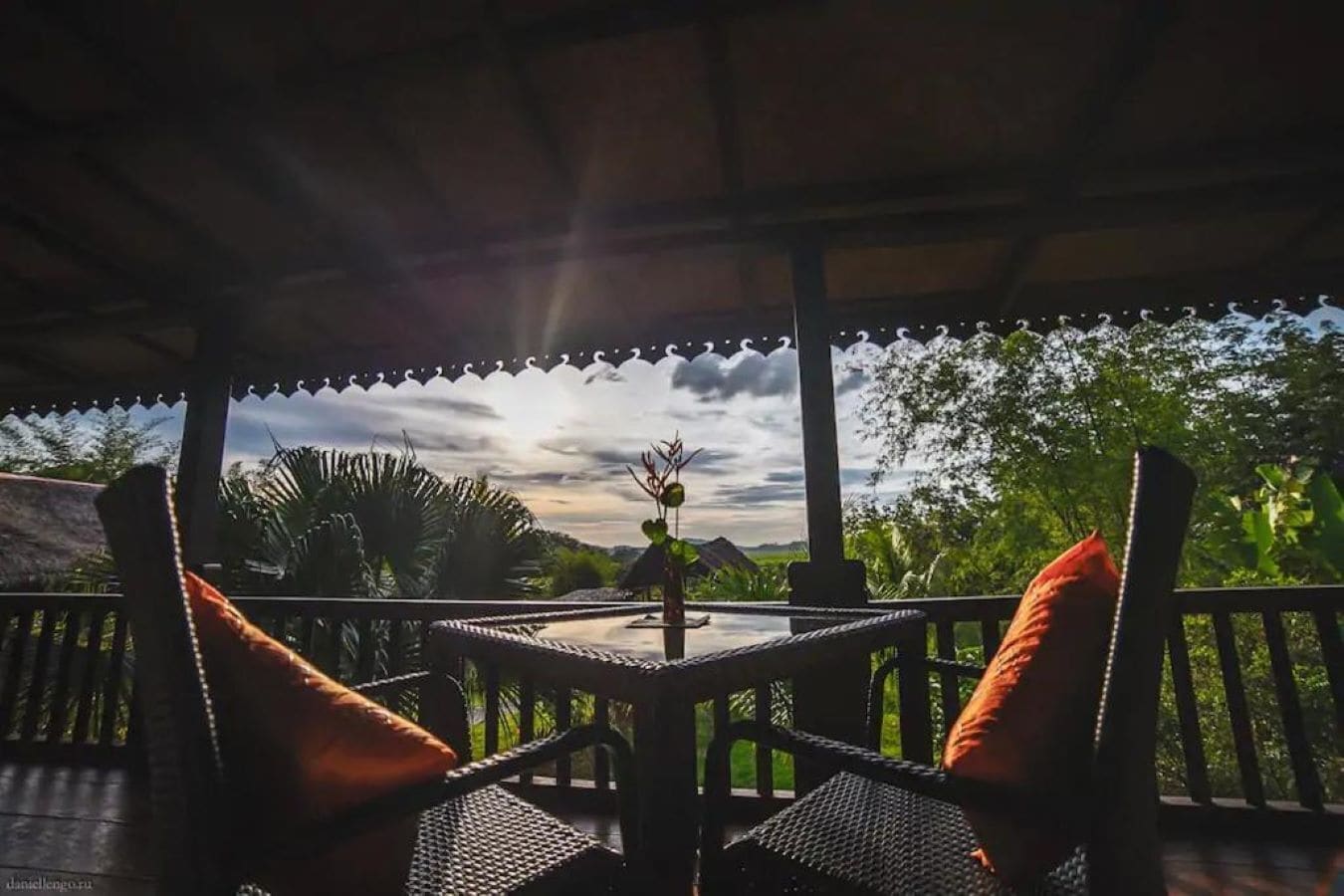 Un espacio de estar al aire libre cubierto con mesa y sillas, rodeado de exuberante vegetación y vistas al cielo.