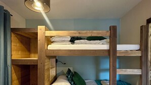 Ett rum med en våningssäng, ett trägolv, en taklampa och ett vägguttag.