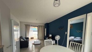 Quarto moderno com mesa de jantar, uma cadeira branca, uma mesinha branca, um ventilador, berço e vista para o exterior.