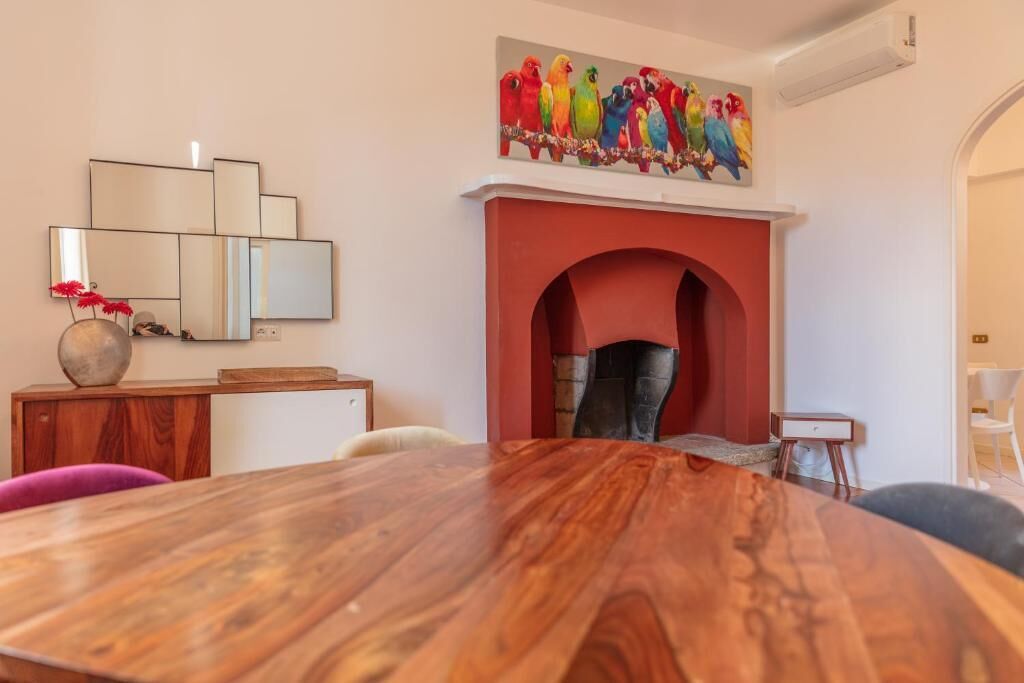 A dining area with a large wooden table, a fireplace, and a colorful bird painting above it.