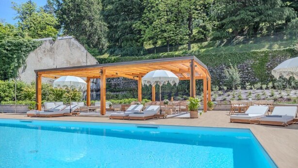 A swimming pool with lounge chairs and umbrellas, surrounded by greenery.