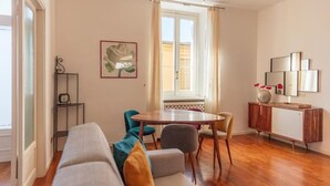 A living room with a sofa, a dining table, chairs, a cabinet, and a window with curtains.