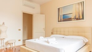 A hotel room with a bed, a painting, a mannequin, and a small stool.