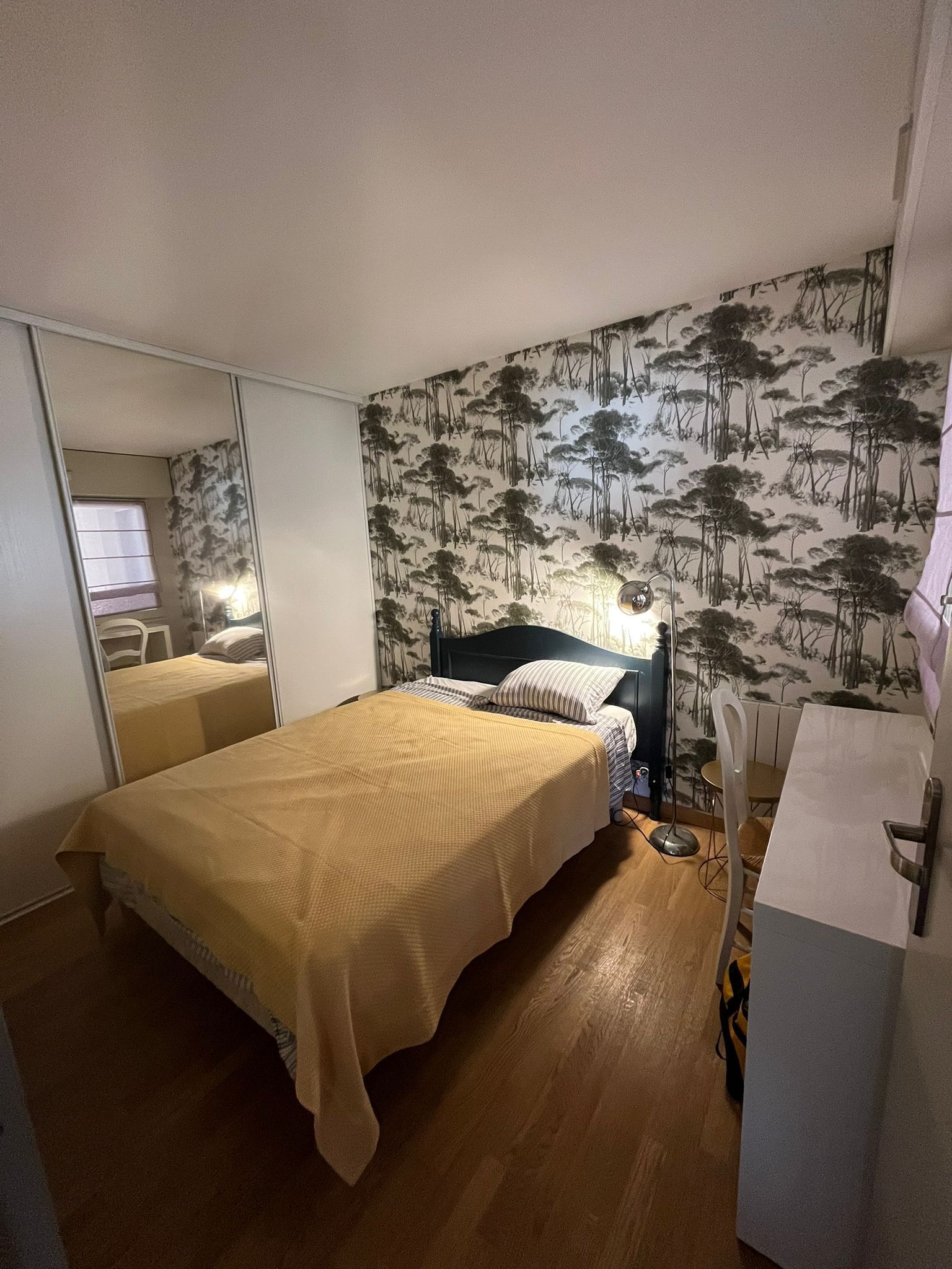 Een slaapkamer met een bed, een spiegel, een dressoir en een muur met een boommotief.