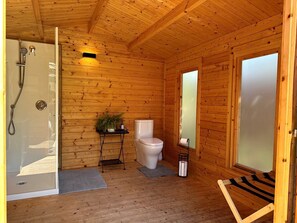 Ein Badezimmer in einer Holzhütte mit Dusche, Toilette und einem kleinen Tisch mit einer Pflanze.