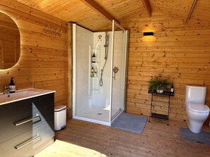 Een houten badkamer in een vakantiehuisje, met een douche, toilet, wastafel en een klein plankje met toiletartikelen.