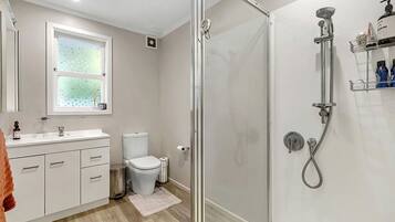 A modern bathroom with a glass shower enclosure, a toilet, a sink with a mirror, and a window.