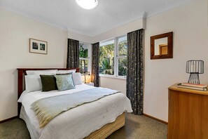 Ein Schlafzimmer mit einem Bett, einem Nachttisch, einer Lampe, einem Fenster mit Vorhängen und einem gerahmten Bild an der Wand.
