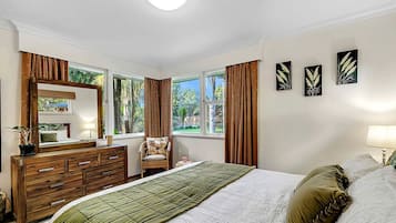 Une chambre à coucher avec un lit, une commode, une chaise et de grandes fenêtres.
