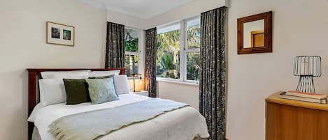 A bedroom with a bed, a bedside table, a lamp, a window with curtains, and a framed picture on the wall.
