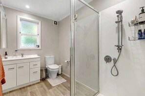 A modern bathroom with a glass shower enclosure, a toilet, a sink with a mirror, and a window.