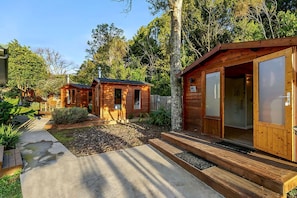 Eine Holzhütte mit einem Betonweg, der zum Eingang führt, umgeben von viel Grün.