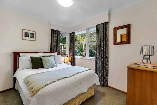 A bedroom with a bed, a bedside table, a lamp, a window with curtains, and a framed picture on the wall.