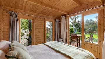 A wooden cabin bedroom with a bed, curtains, and a view of the outdoors.