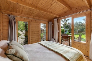A wooden cabin bedroom with a bed, curtains, and a view of the outdoors.