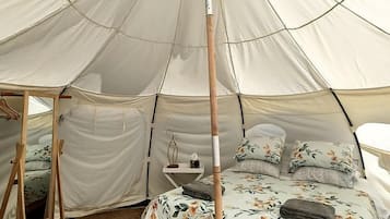A tent with a bed inside, a wooden stand, and a small table with a lamp.