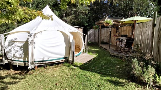 A tent with a covered patio area, a hanging planter, and a wooden deck. - Luxury Hillside Glamping with Outdoor Kitchen near Waiheke Island, New Zealand (Auckland)