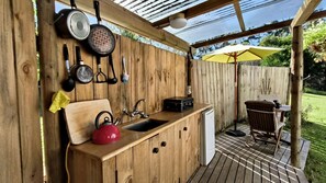 A wooden outdoor kitchen with a sink, kettle, and various cooking utensils.