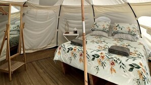 A tent with a bed inside, a wooden stand, and a small table with a lamp. - Luxury Hillside Glamping with Outdoor Kitchen near Waiheke Island, New Zealand (Auckland)