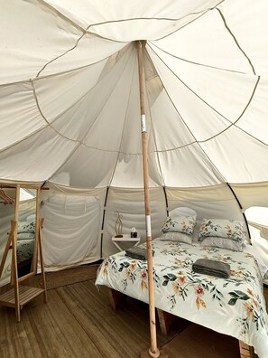 A tent with a bed inside, a wooden stand, and a small table with a lamp.