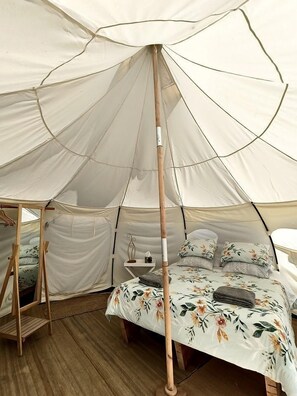 A tent with a bed inside, a wooden stand, and a small table with a lamp.