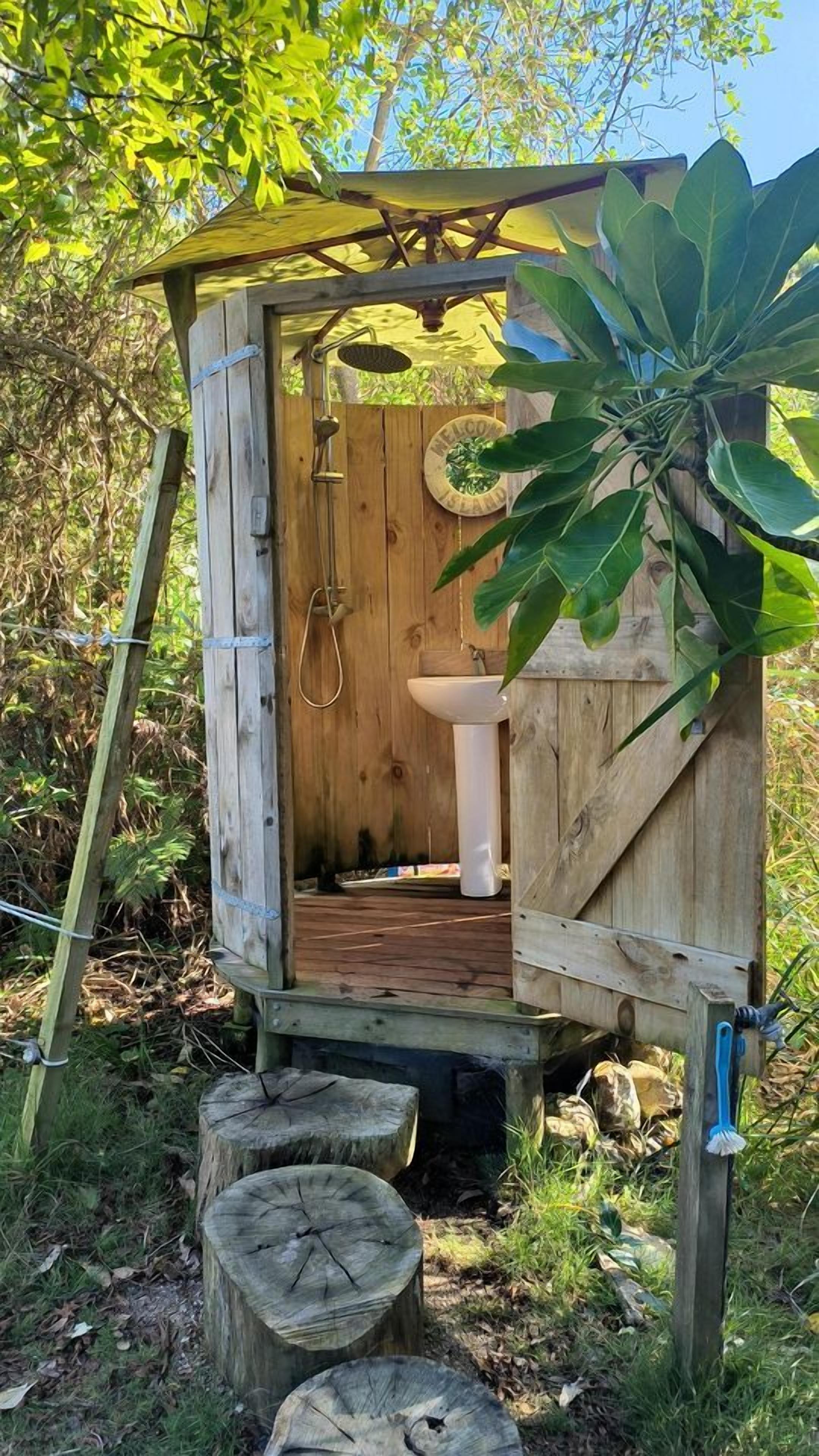 A wooden outhouse with a door, a sink, and a shower.