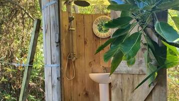 A wooden outhouse with a door, a sink, and a shower.