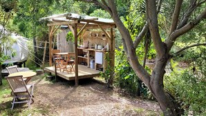 A wooden structure with a table and chairs, surrounded by trees. - Secluded Island Glamping Retreat with Outdoor Kitchen and Private Bathroom near Oneroa, Waiheke Island (Isla Waiheke)