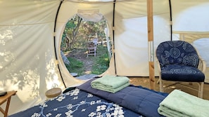 Ein Zelt mit Bett, Stuhl und Blick auf einen Außenbereich mit Tisch und Stühlen.