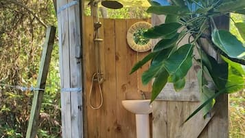 En liten utedass av trä med dörr, handfat och dusch.