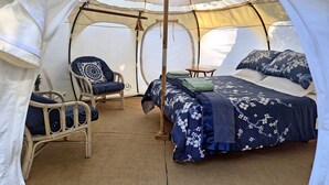 A tent with a bed, a chair, and a small table. - Secluded Island Glamping Retreat with Outdoor Kitchen and Private Bathroom near Oneroa, Waiheke Island (Isla Waiheke)