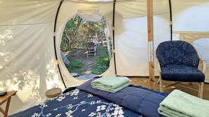Une tente équipée d’un lit, d’une chaise et offrant une vue sur un espace extérieur aménagé avec une table et des chaises.