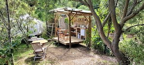 Eine Holzhütte mit Tisch und Stühlen, umgeben von Bäumen.