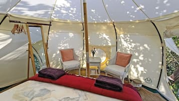 A tent with a bed, two chairs, a small table, and a hanging rack.