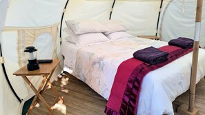 A tented room with a bed, pillows, a table with a lantern, and a blanket. - Sunny Vineyard-View Glamping with Outdoor Kitchen near Oneroa, Waiheke Island (Isla Waiheke)