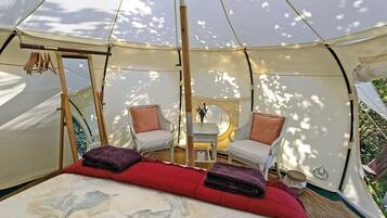 A tent with a bed, two chairs, a small table, and a hanging rack.