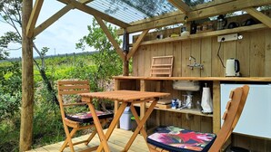A wooden outdoor kitchen with a table and chairs, a sink, and a refrigerator.