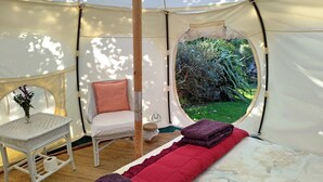 Une tente équipée d’un lit, d’une chaise, d’une petite table et offrant une vue sur la verdure environnante.