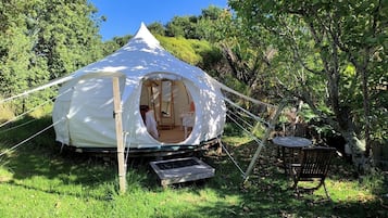 A white tent with an open entrance, surrounded by greenery and trees.