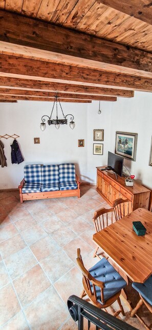 A rustic interior with a wooden ceiling, a checkered sofa, a dining table with chairs, and a television on a wooden cabinet. - Liana's home in Letino (Letino)