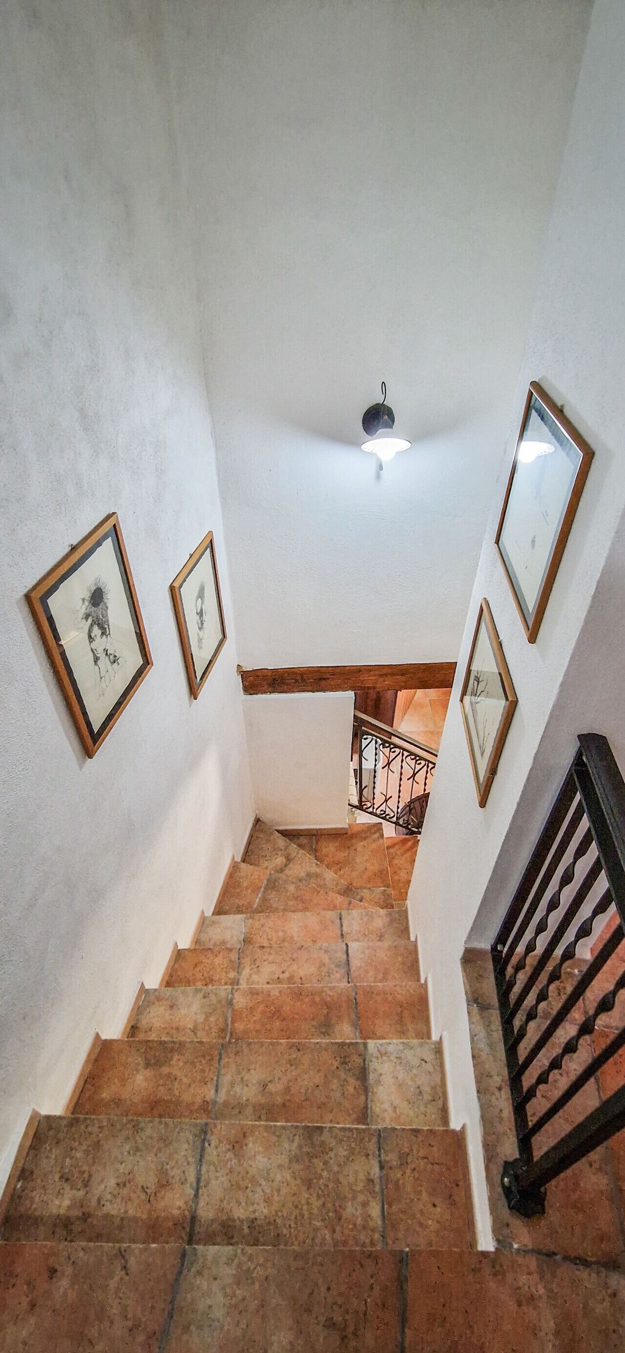 Un escalier avec des marches en pierre, des murs blancs et des tableaux encadrés.