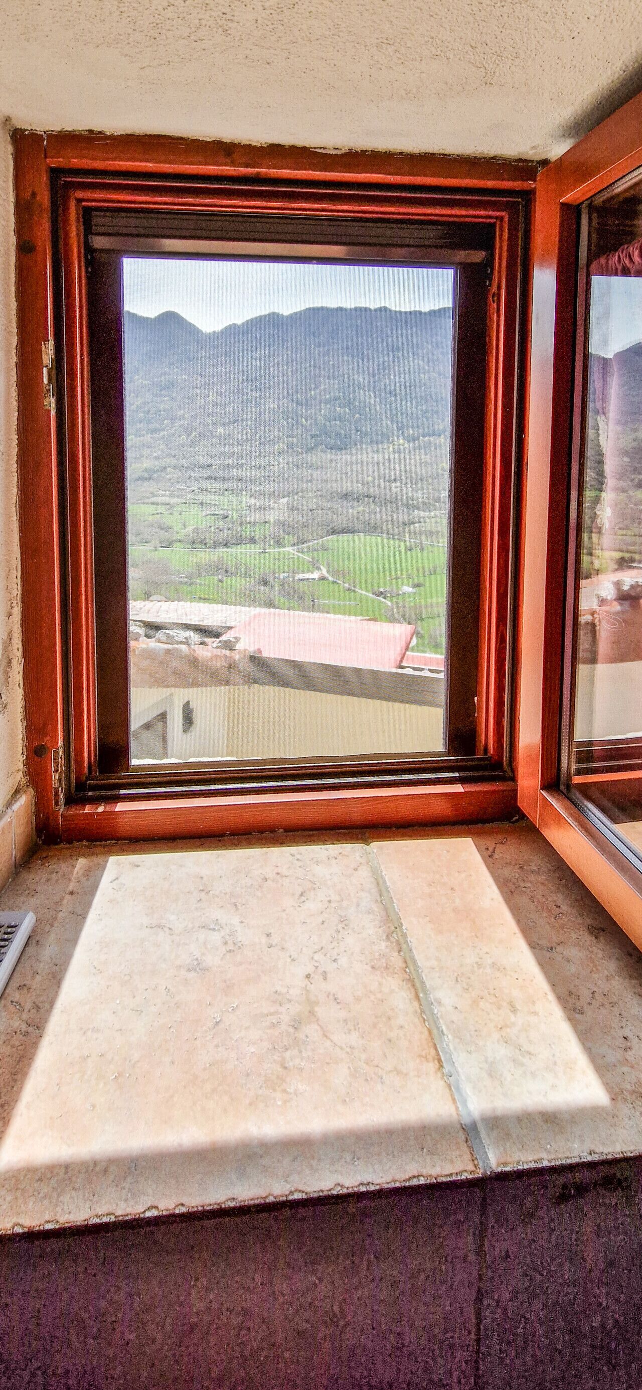 Une fenêtre donnant sur un paysage montagneux et un bâtiment avec un toit rouge.