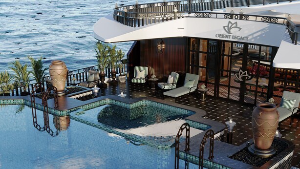 Zona de piscina con vistas al mar, sillas de descanso y un edificio con el letrero 'ORIENT LEGACY'.