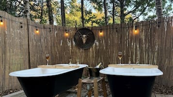 Two black bathtubs on a wooden deck with a wooden fence and a deer skull decoration in the background.